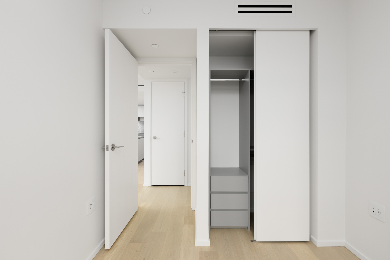 A modern, empty room with light wood flooring, an open closet with shelves, and two open white doors leading to a hallway and another room.
