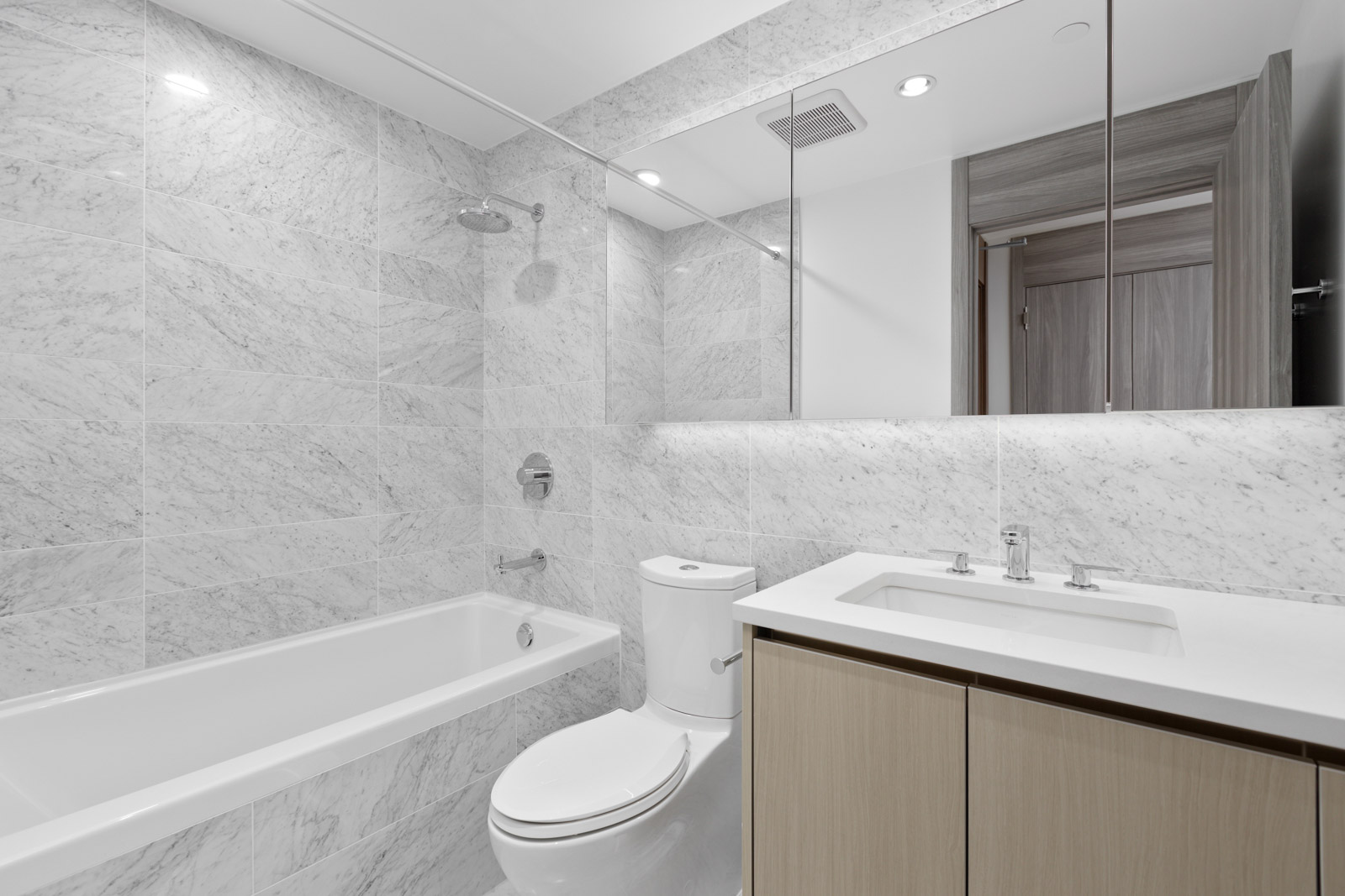 marble design washroom with soaker tub, toilet and sink with under cabinet space. All white and large mirror.