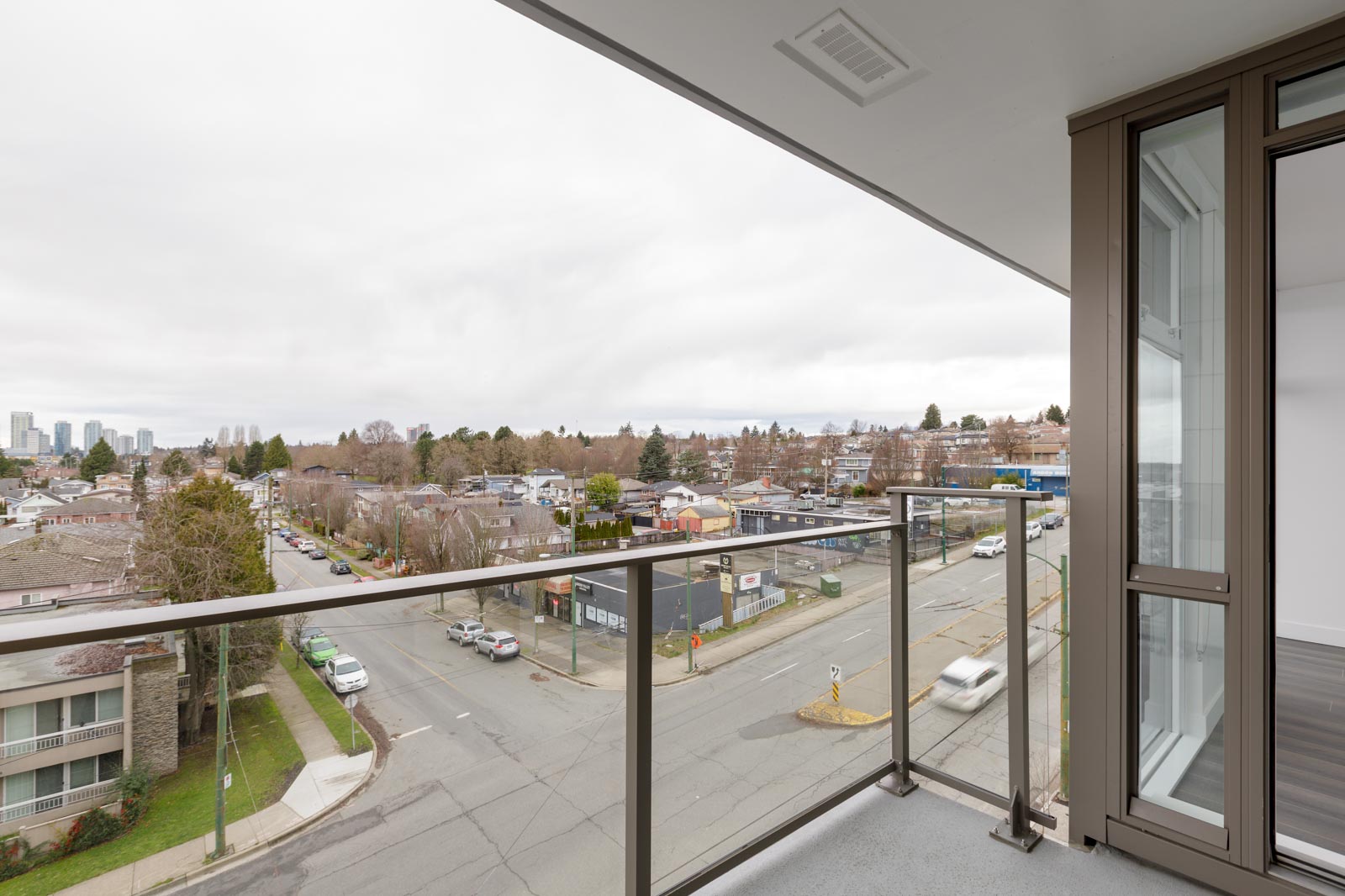 View from a balcony overlooking a street intersection with buildings, cars, and trees under a cloudy sky.