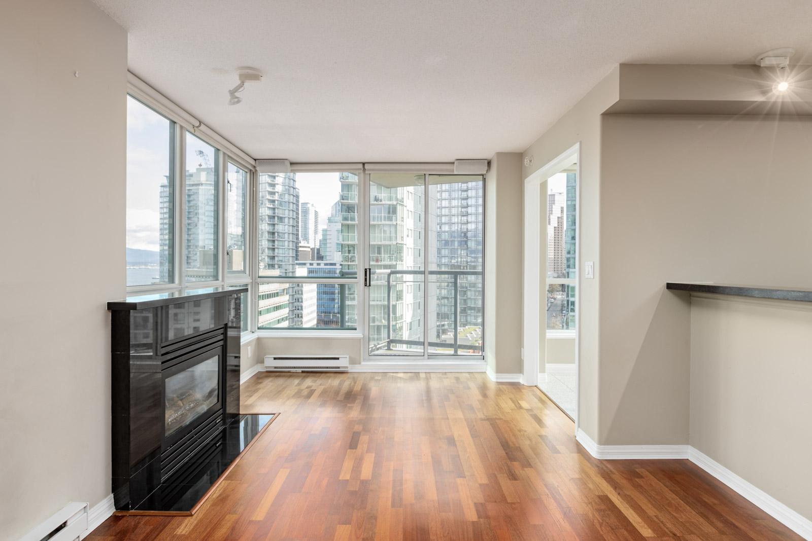Empty modern apartment living room with hardwood floors, a fireplace, large windows, and a balcony with city views.