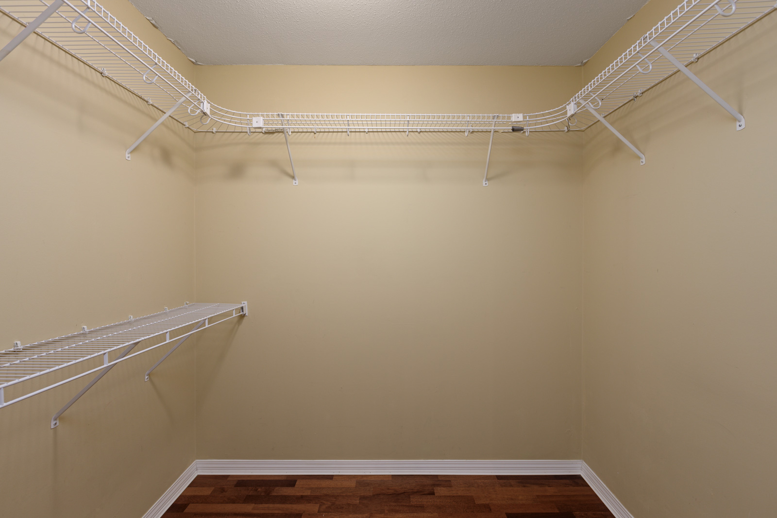 Empty walk-in closet with beige walls, wooden floor, and white wire shelving along the sides and back walls.