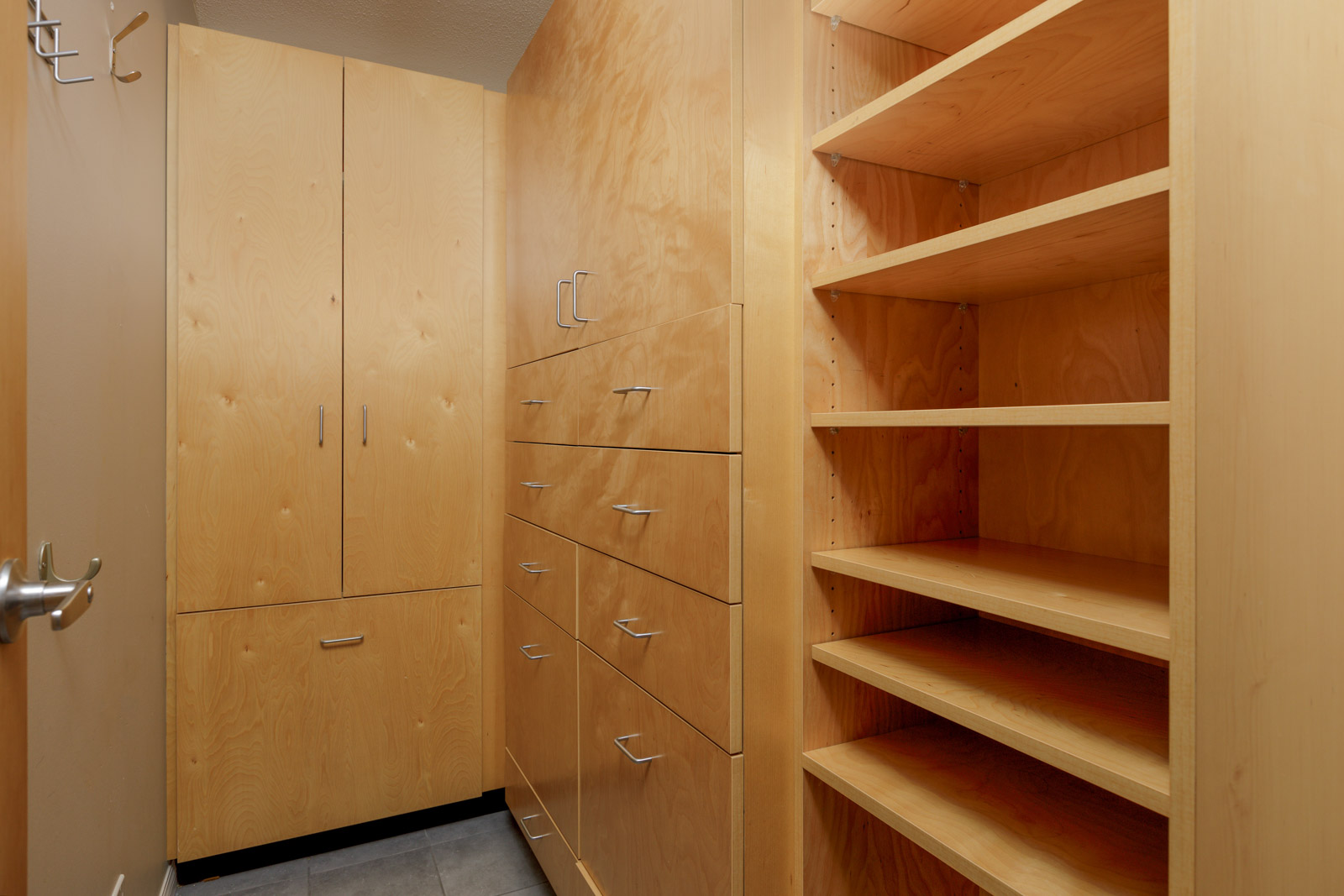 Small walk-in closet with light wood cabinets, several drawers with metal handles, tall storage compartments, and open shelving on the right.