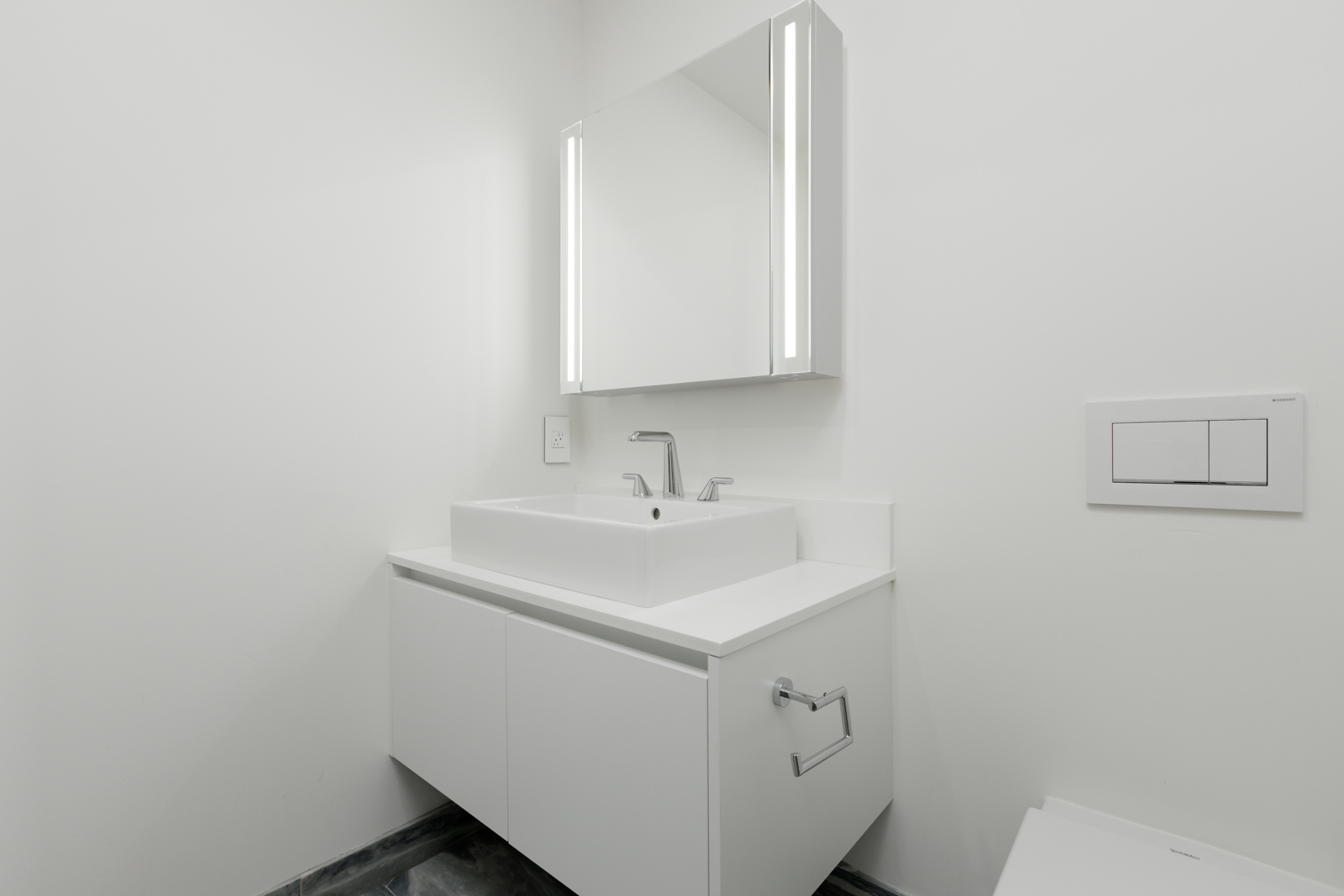 Minimalist white bathroom with a floating vanity, rectangular sink, mirror with built-in lights, and a wall-mounted dual flush toilet.