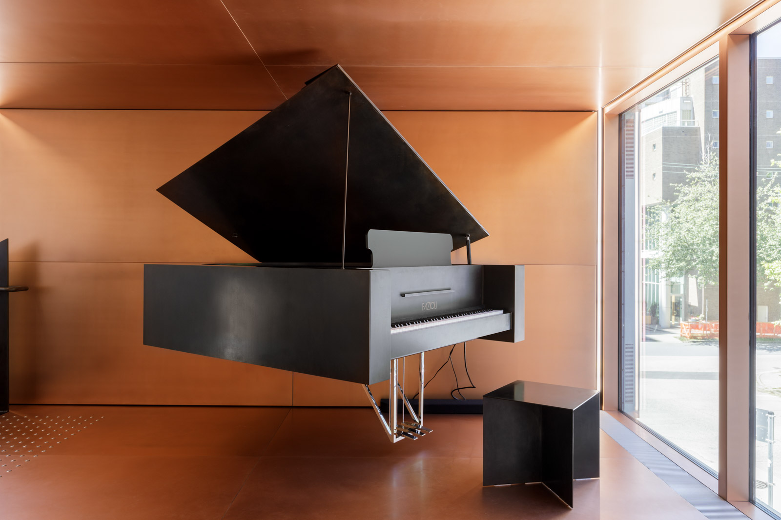 A modern black grand piano appears to float above the floor in a minimalist, copper-toned room with large windows.