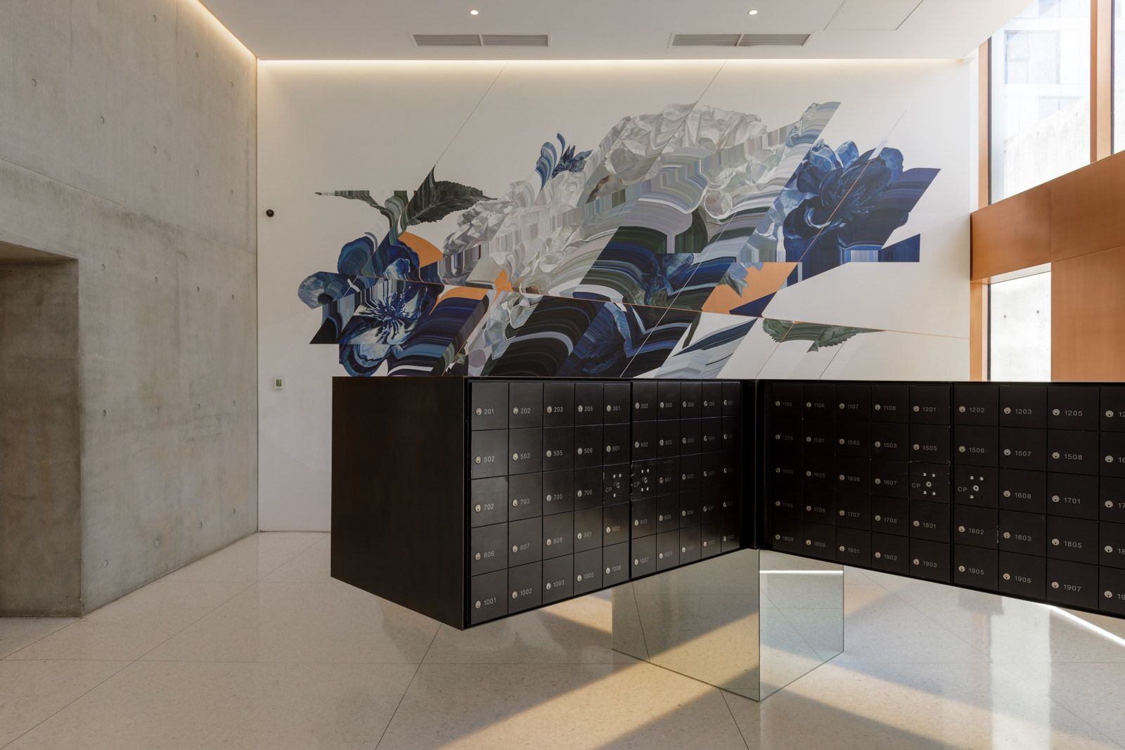 A modern lobby with black mailboxes, a glass cube on a tiled floor, and a large abstract mural on the wall.