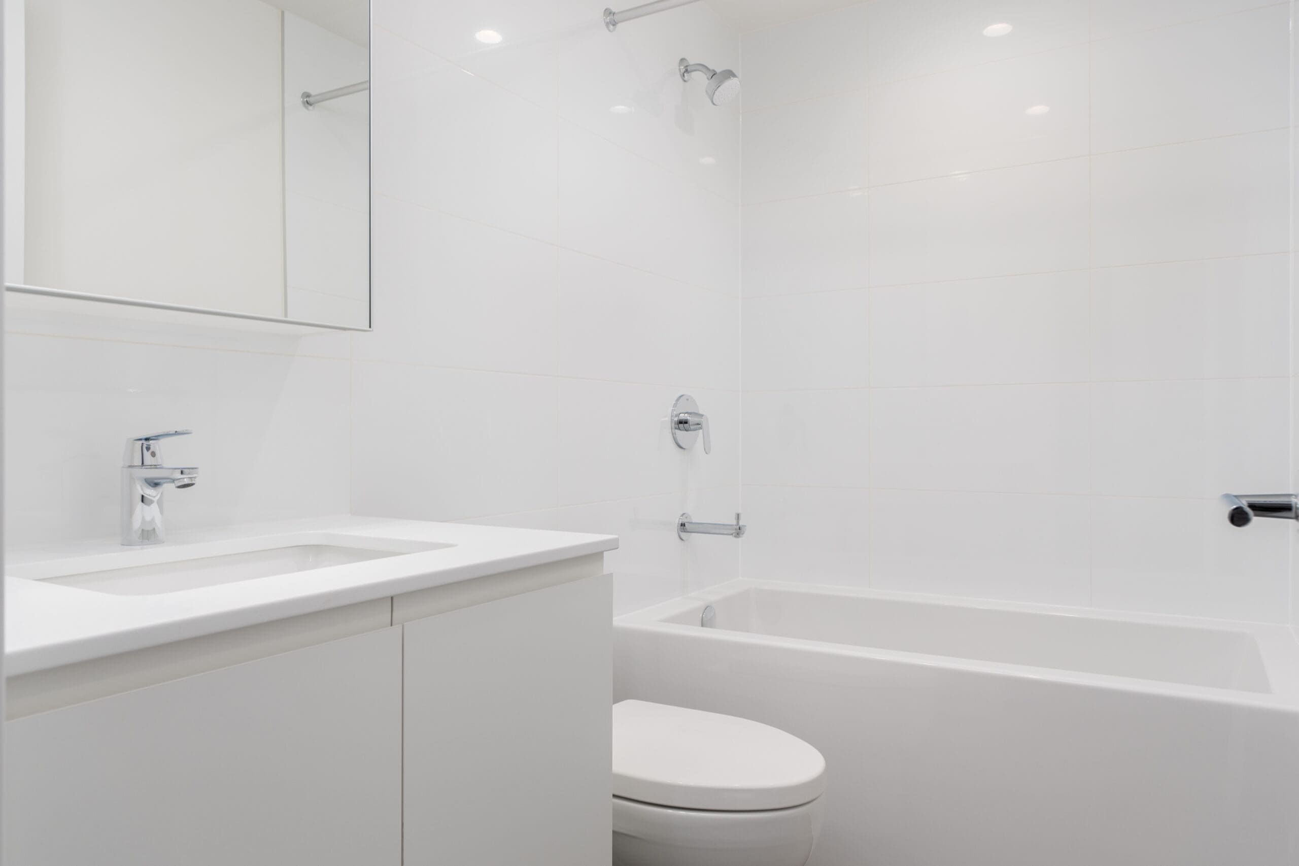 A modern white bathroom with a sink, faucet, mirror, toilet, and bathtub with a showerhead.