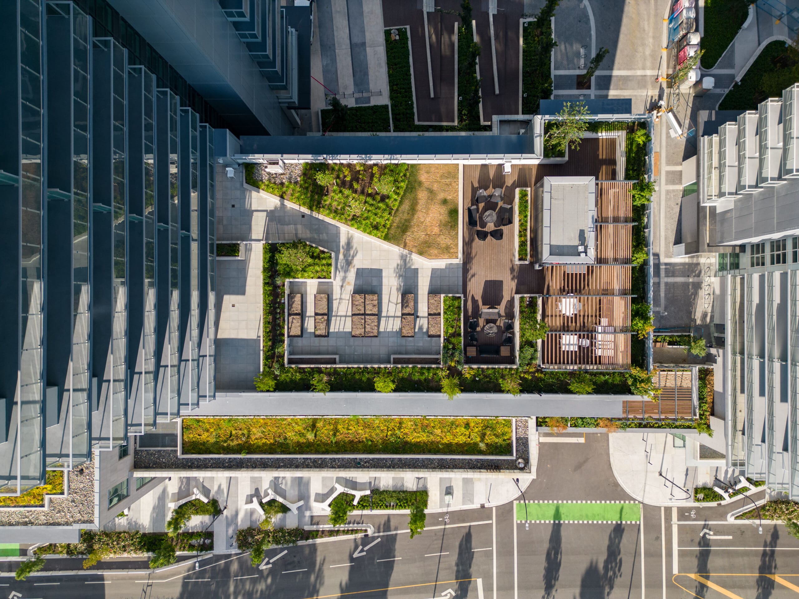Aerial view of a modern rooftop terrace with seating areas, greenery, pathways, and adjacent city streets.