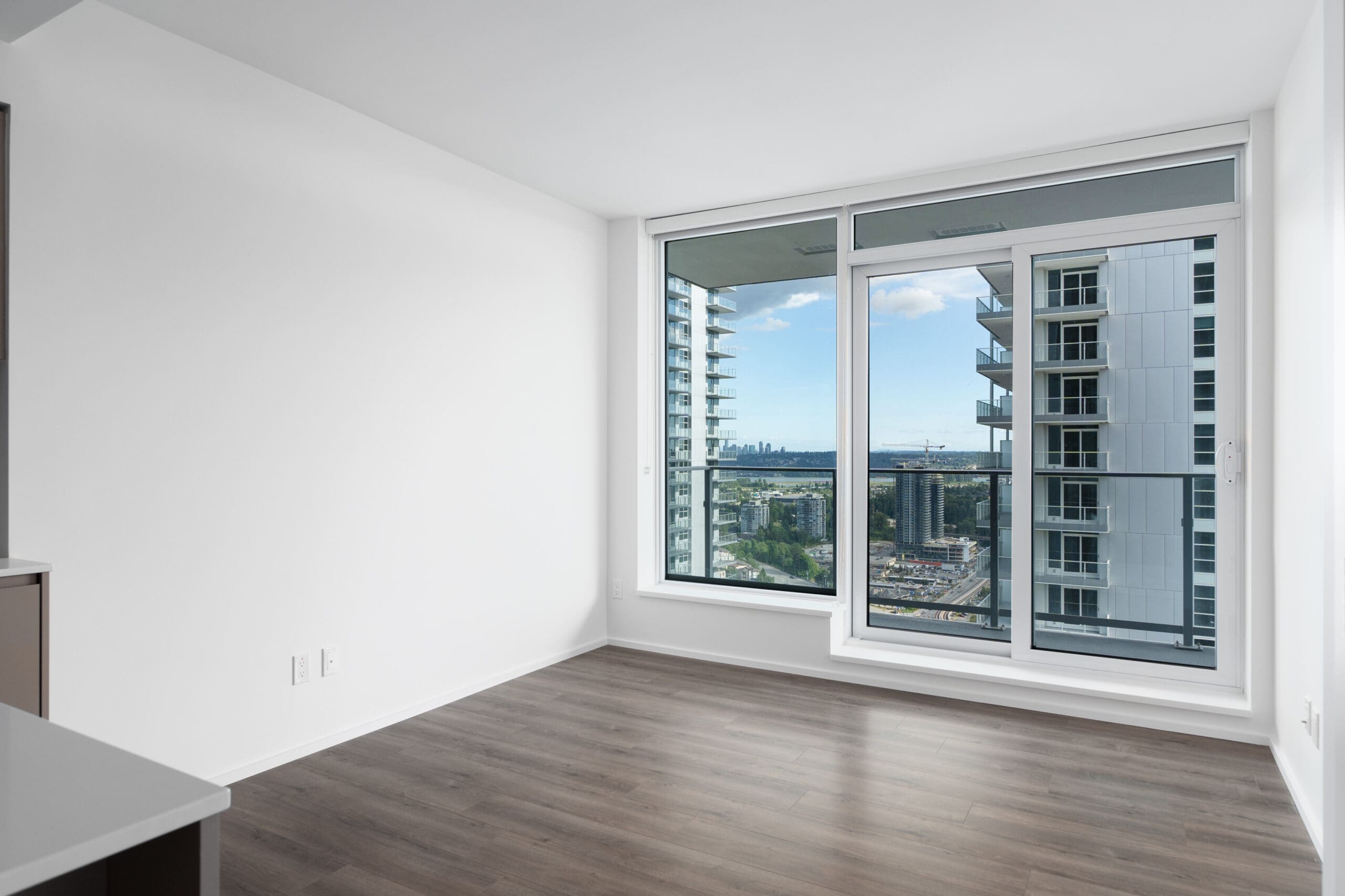 Unfurnished apartment room with large floor-to-ceiling window, glass balcony door, and a view of nearby high-rise buildings and cityscape.