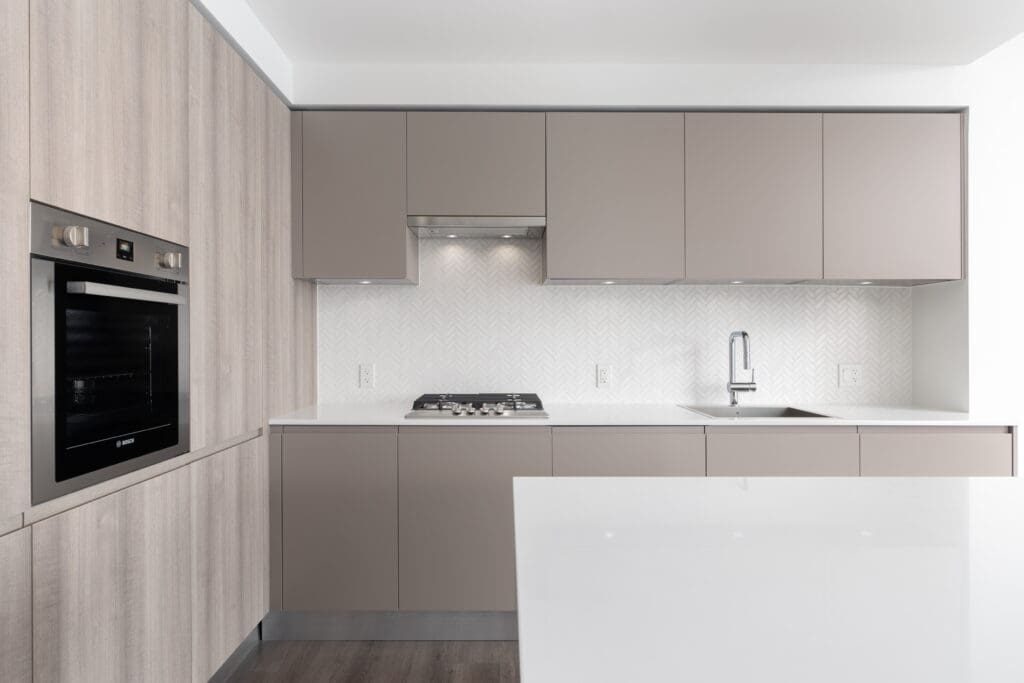 Modern kitchen with built-in oven, gas cooktop, sink, light wood and beige cabinets, white countertop, and herringbone tile backsplash.
