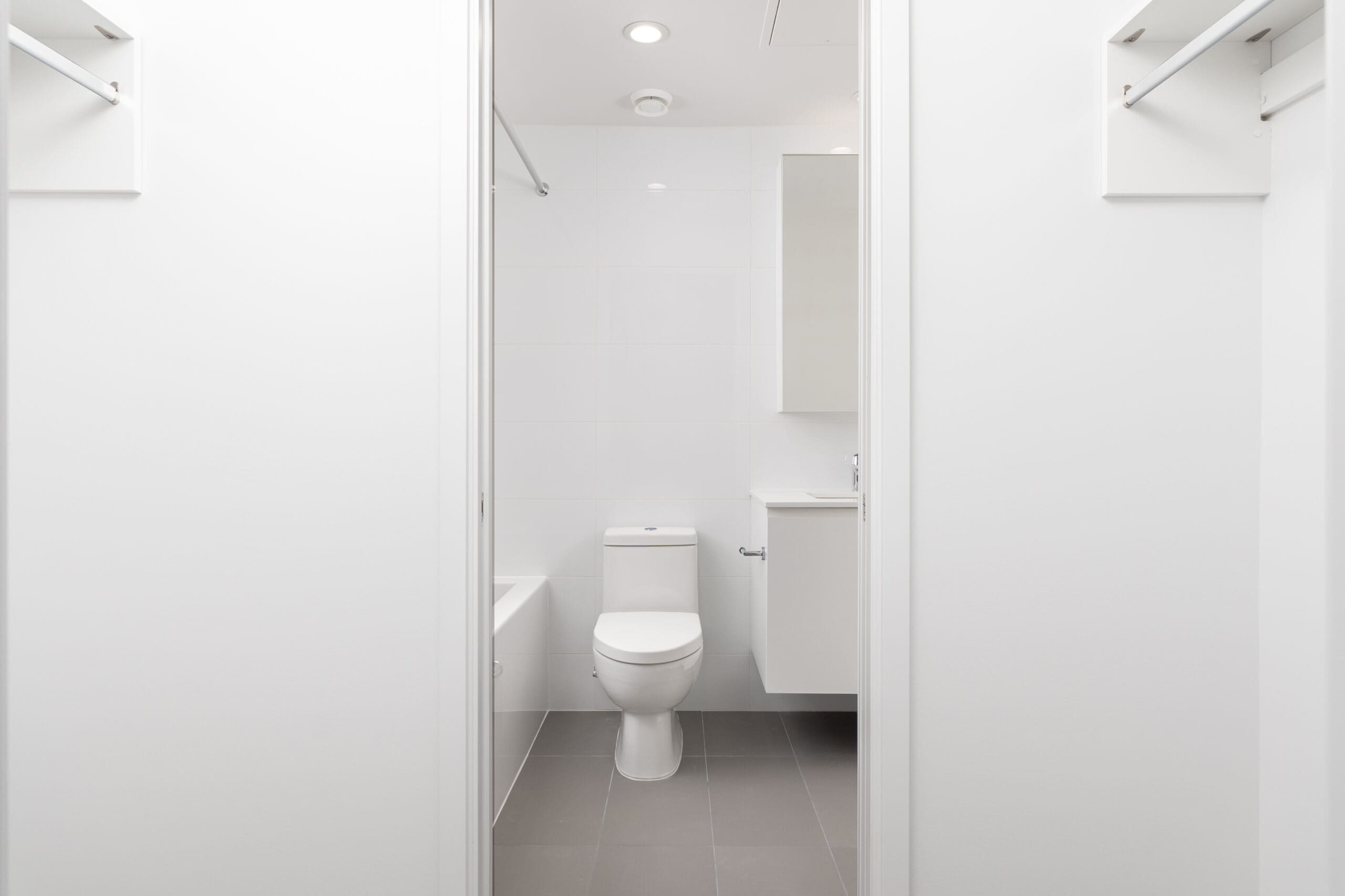 A modern, minimalistic bathroom with a white toilet, white vanity, bathtub, and light gray floor tiles.