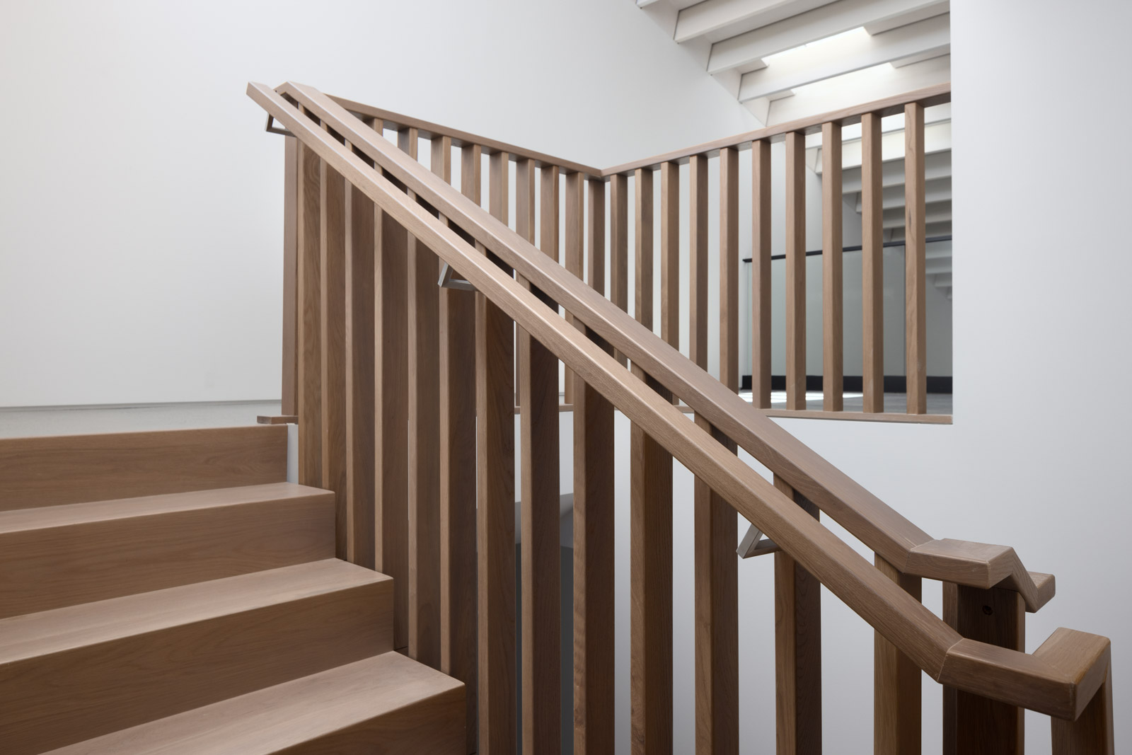 A modern indoor staircase with wooden steps and railings, set against white walls and a ceiling with exposed beams.