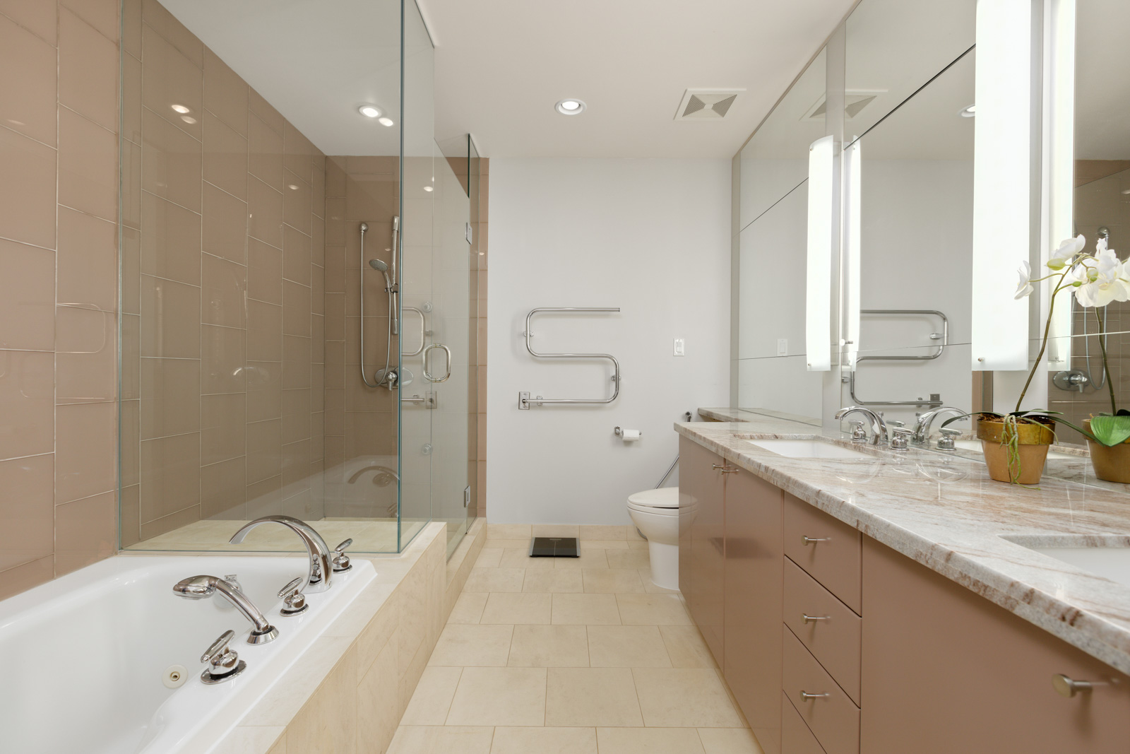 Modern bathroom with beige tile floor, bathtub with built-in faucets, glass shower, wall-mounted toilet, double sink vanity, and large mirrors.