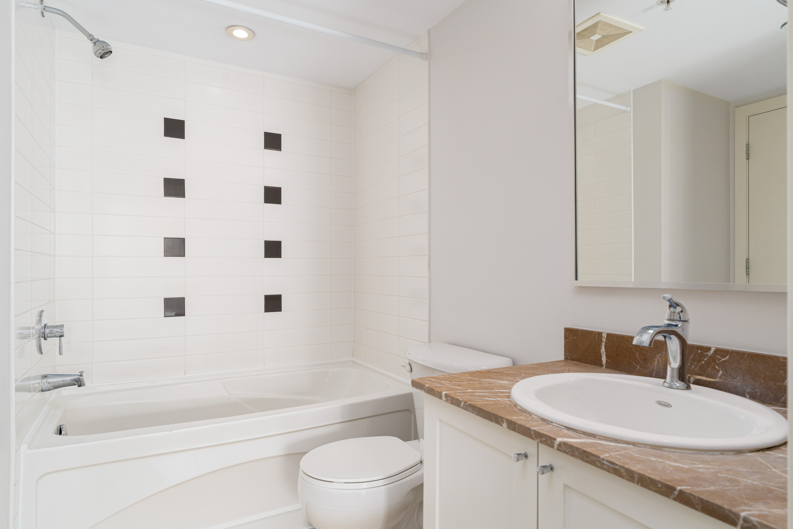 Modern bathroom with a white bathtub, toilet, brown countertop with sink, and a tiled wall featuring a pattern of black and white tiles.