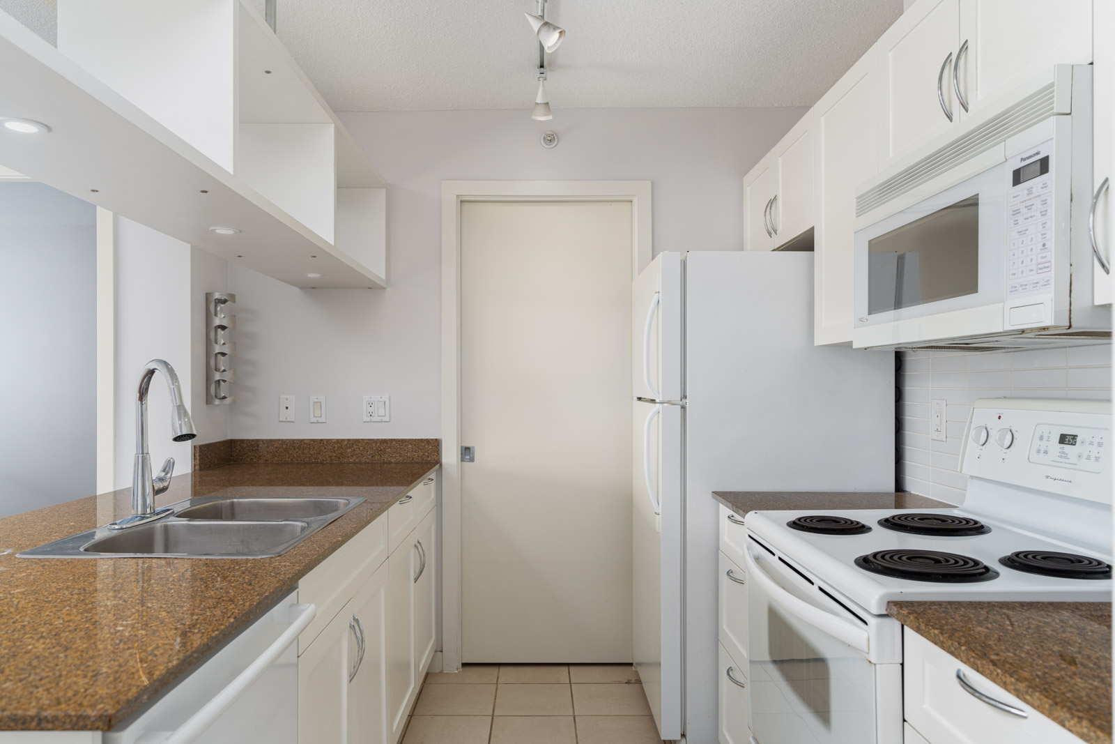 Modern kitchen with white cabinets, brown countertops, a double sink, white appliances including a fridge, stove, and microwave, and neutral tile flooring.