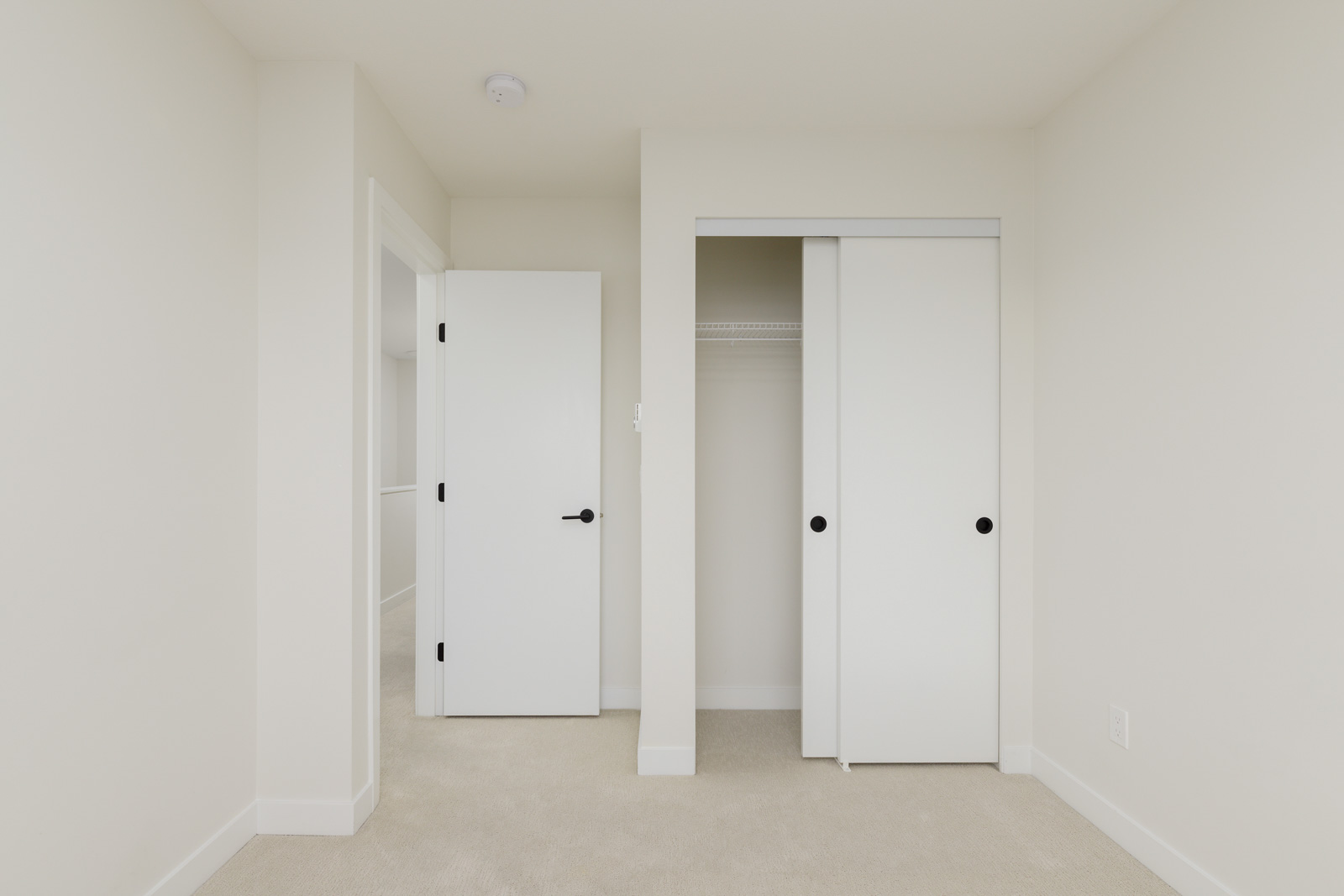 Small empty room with beige carpet, white walls, an open door, and a closet with sliding white doors.