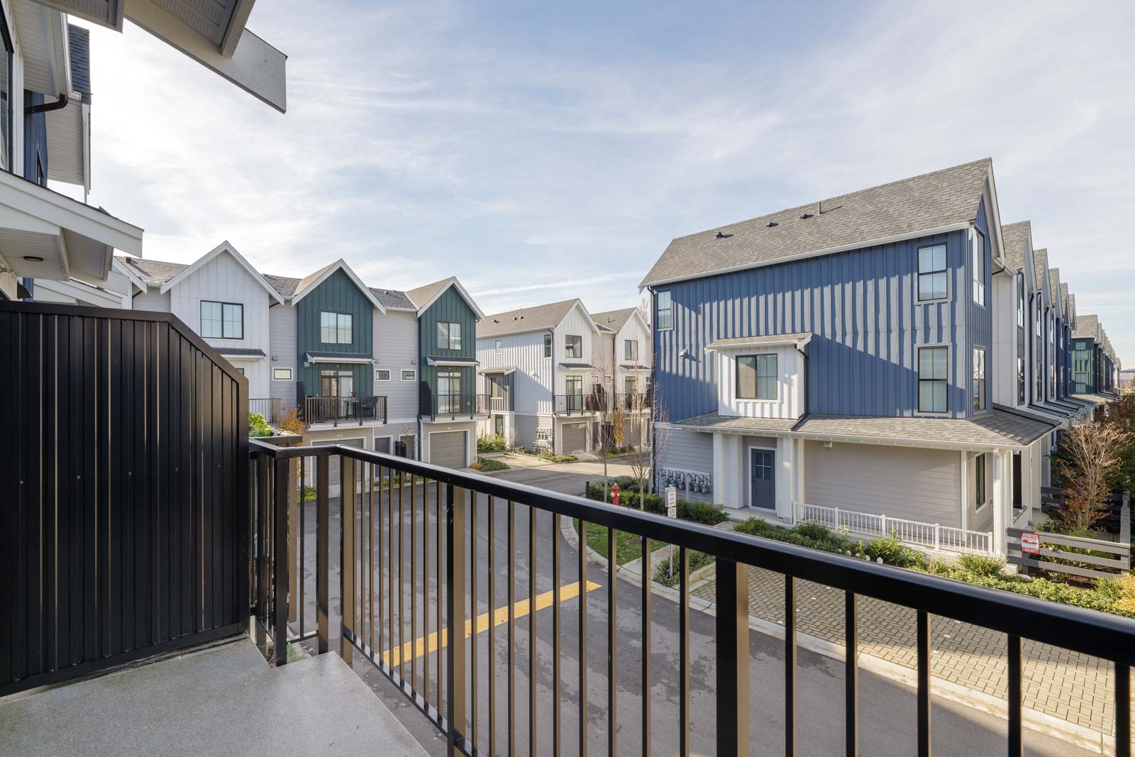 View from a balcony overlooking a residential neighborhood with modern townhouses, featuring pitched roofs and neutral-colored exteriors on a clear day.