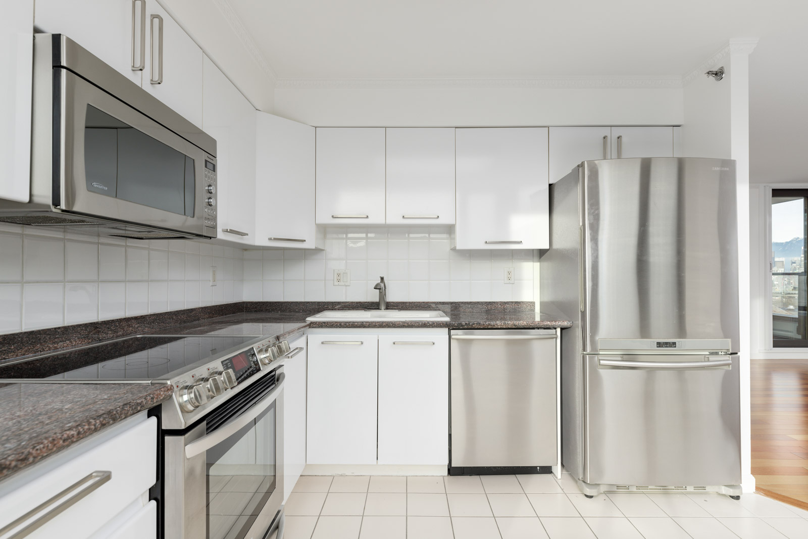 Modern kitchen with white cabinets, stainless steel appliances including a refrigerator, stove, microwave, and dishwasher, and dark granite countertops.