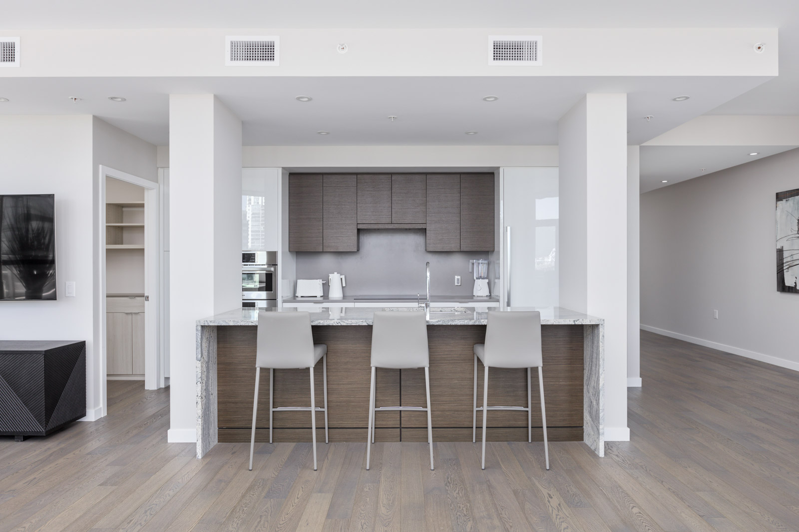 Modern kitchen with a marble island, three gray bar stools, built-in cabinets, and integrated appliances in a bright, open-plan apartment.