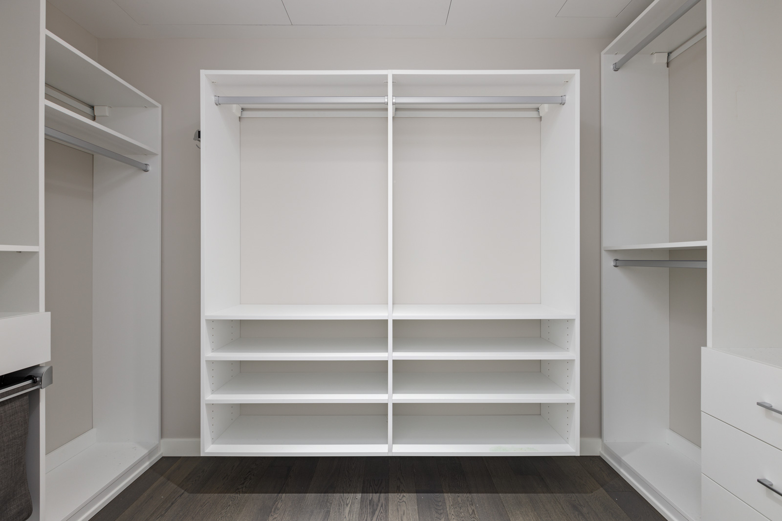 Empty white walk-in closet with open shelves, hanging rods, and dark wood flooring. No items are stored in the closet.