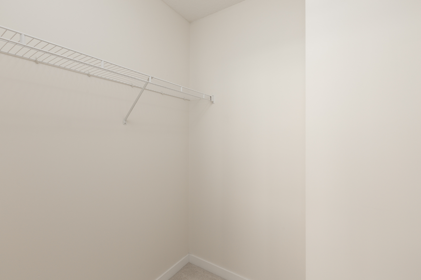 Empty walk-in closet with beige walls, white baseboards, and a single white wire shelf mounted on the left wall.