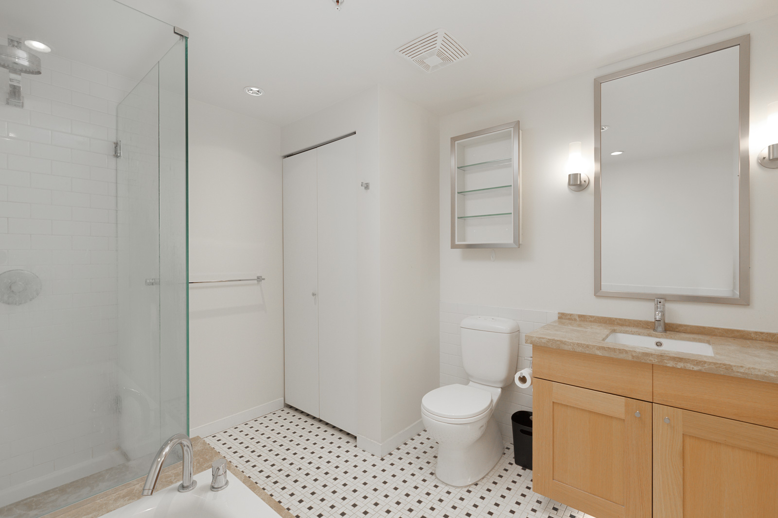 Modern bathroom with glass shower, bathtub, toilet, wood vanity with sink, large mirror, white walls, and tiled floor.