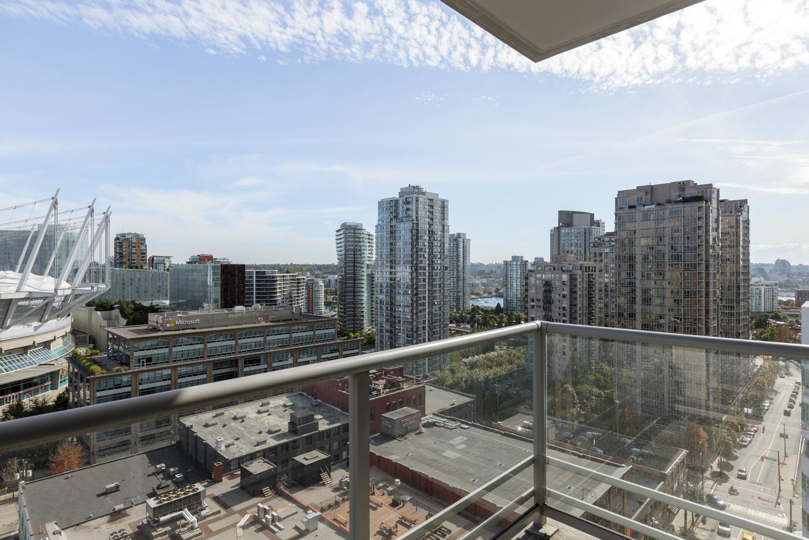 View from a high-rise balcony overlooking a cityscape with multiple modern buildings, a stadium on the left, and a partly cloudy sky.