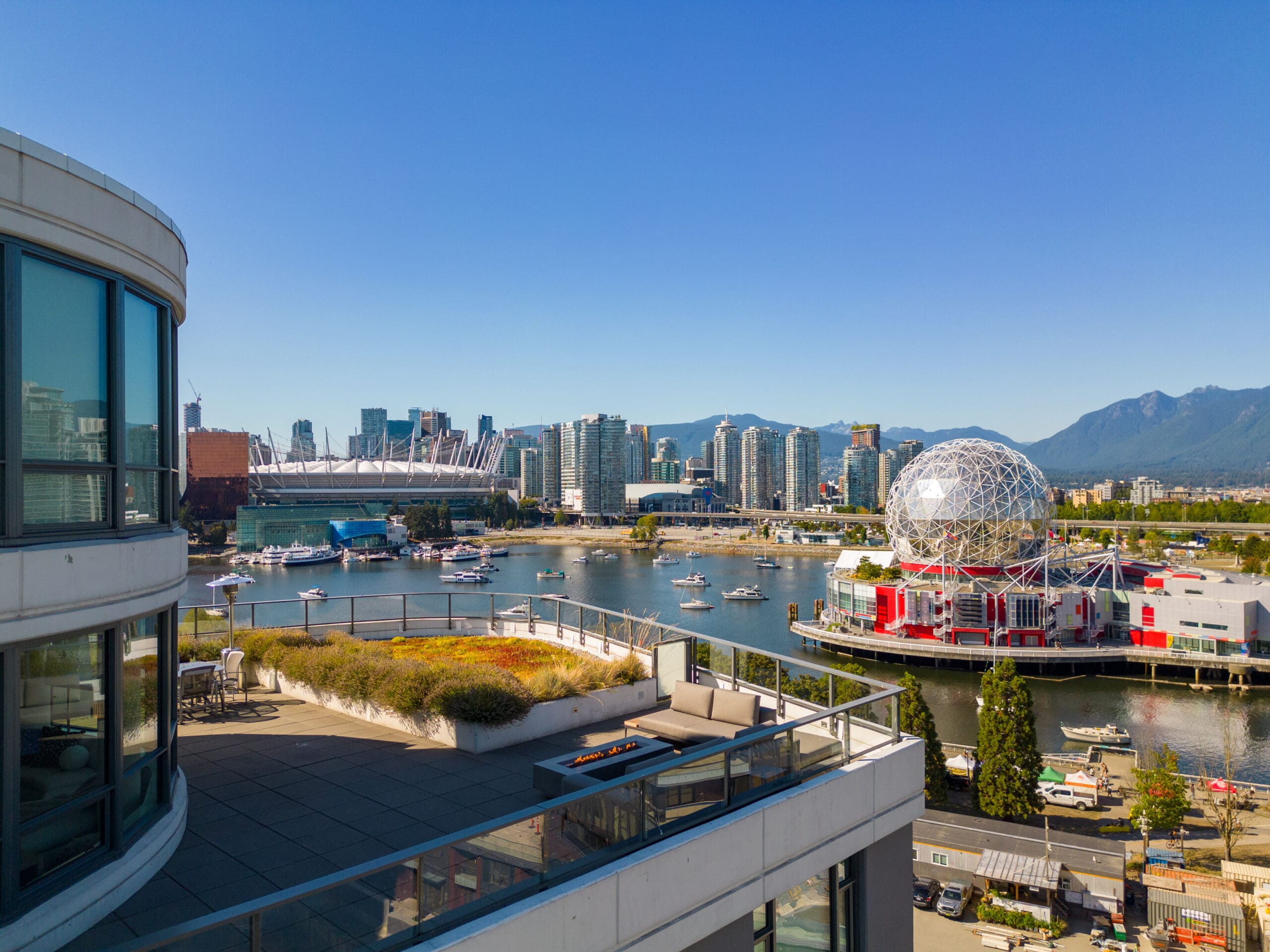View of Vancouver skyline with modern buildings, Science World geodesic dome, and waterfront on a clear day, seen from a rooftop terrace.