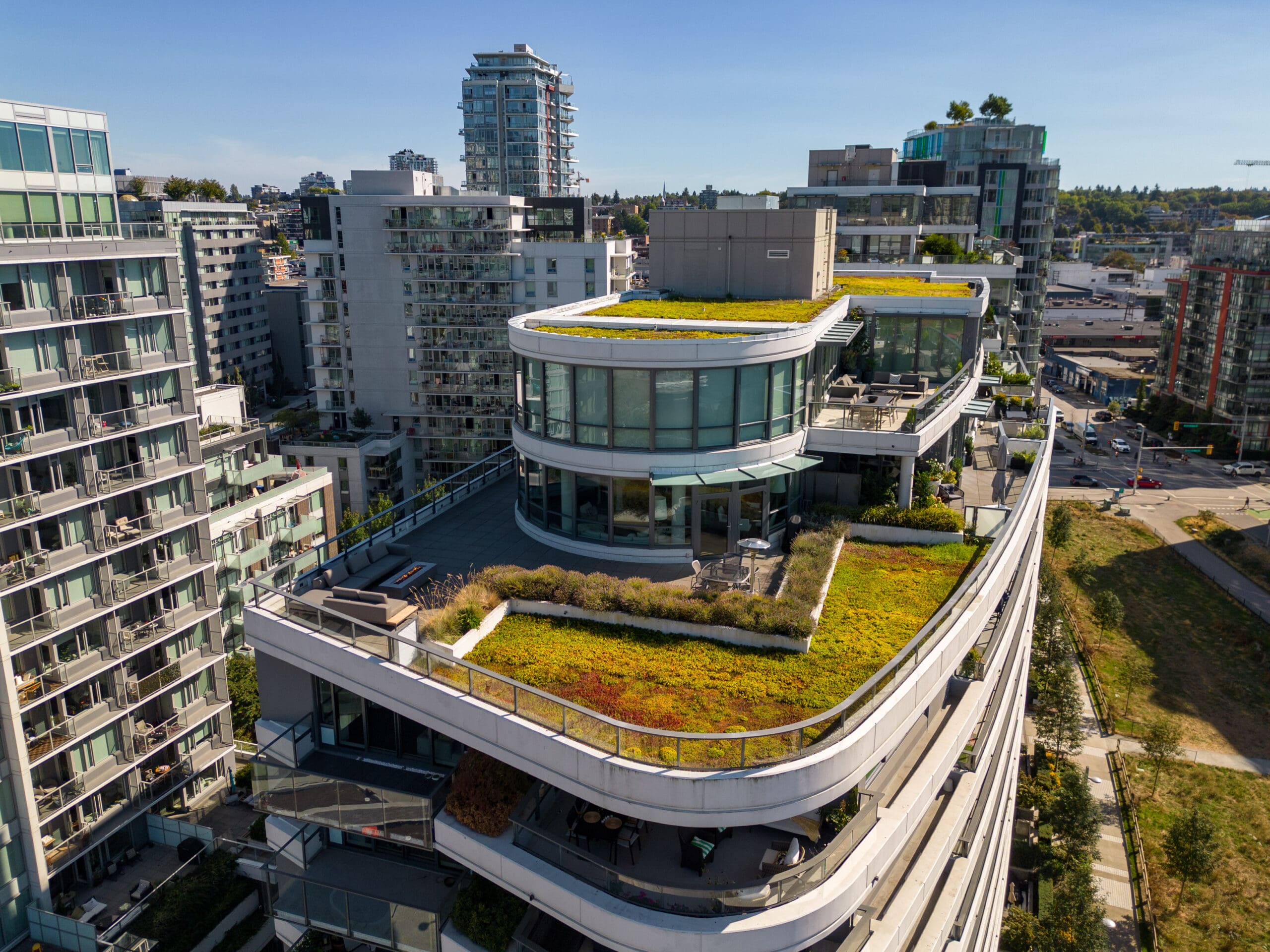 Aerial view of a modern multi-story building with extensive green roofs, surrounded by other high-rise buildings in an urban area.