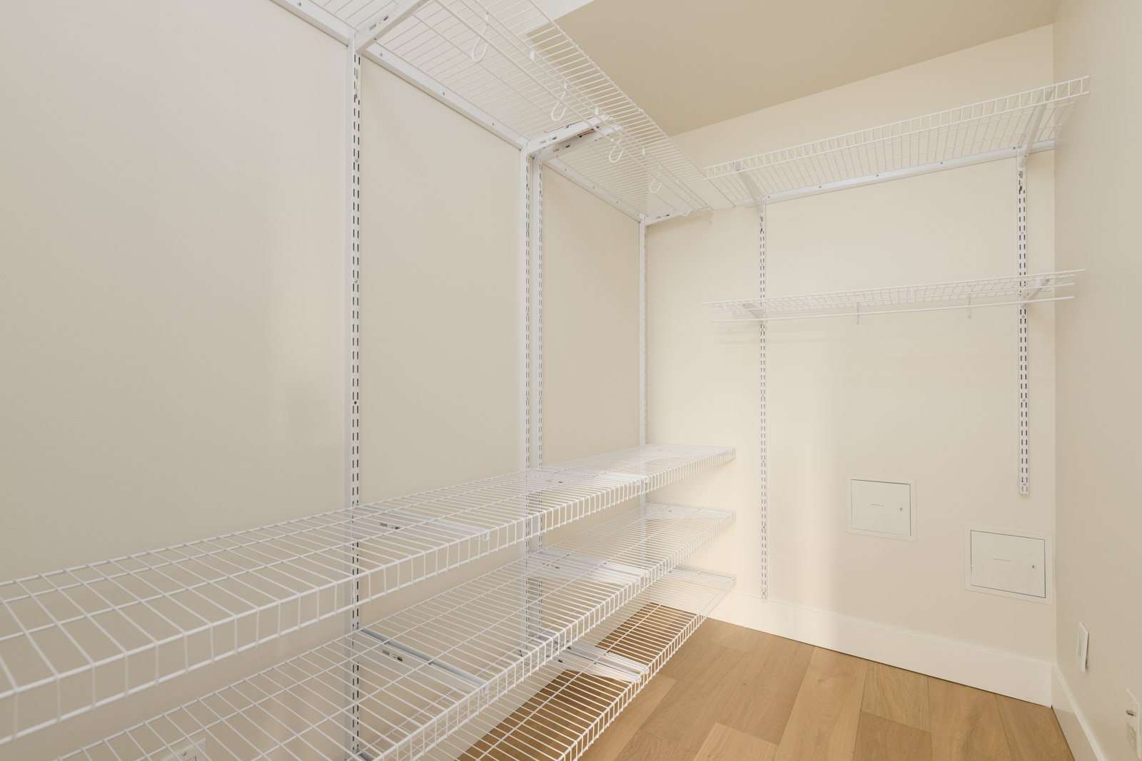 Empty walk-in closet with white wire shelving on three walls and light wood flooring.