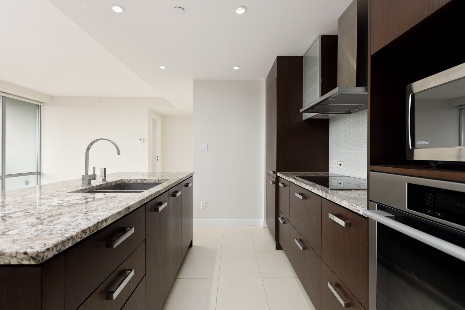 Modern kitchen with dark wood cabinets, granite countertops, stainless steel appliances, and a central island with a sink under recessed lighting.