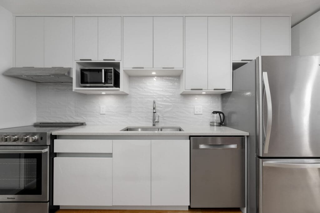 Modern kitchen with white cabinets, stainless steel appliances, a sink under a central light, and a white textured backsplash.