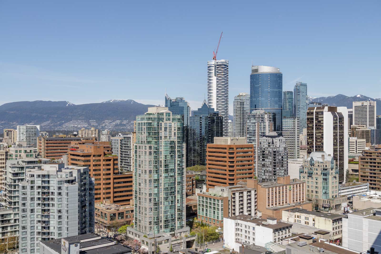 Downtown cityscape with modern high-rise buildings under a clear sky; mountains are visible in the background.