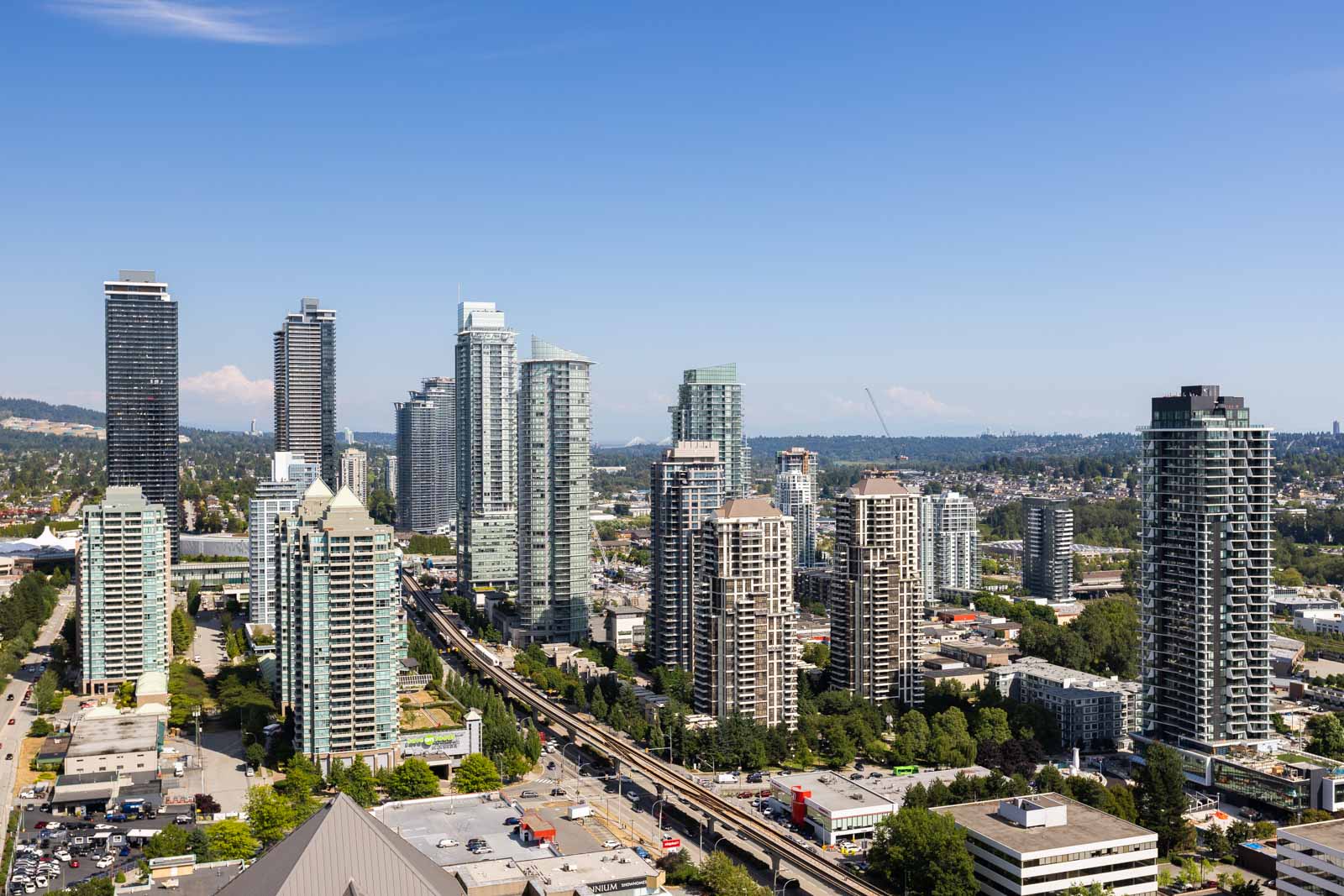 A cityscape with modern high-rise buildings, a light rail track running through the center, and clear blue sky above.