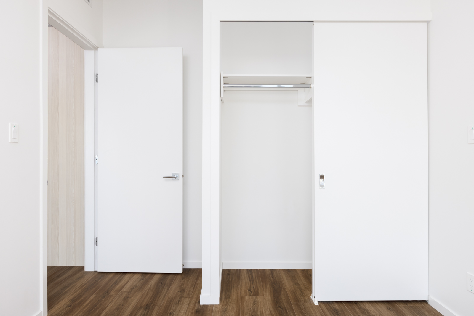 Empty room with a wood floor, open white door on the left, and an open closet with sliding white doors on the right.