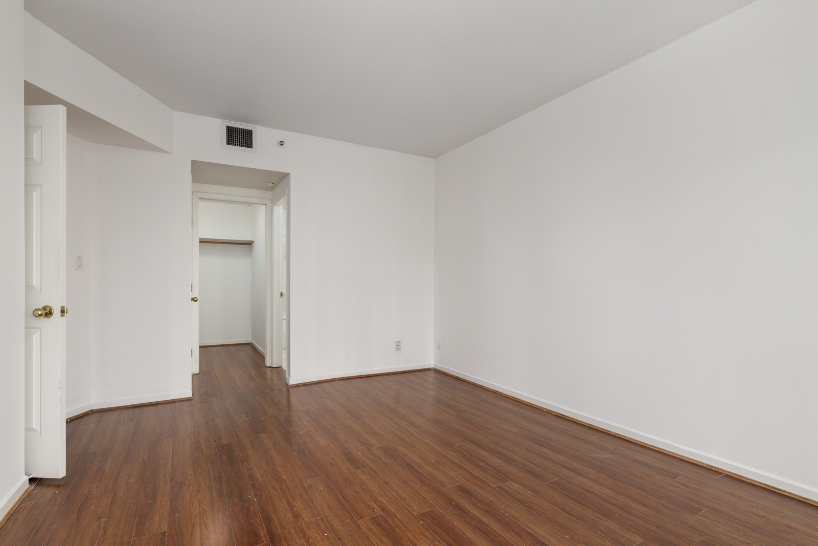 Empty room with white walls, wood flooring, an open door, a visible closet, and ceiling vent.