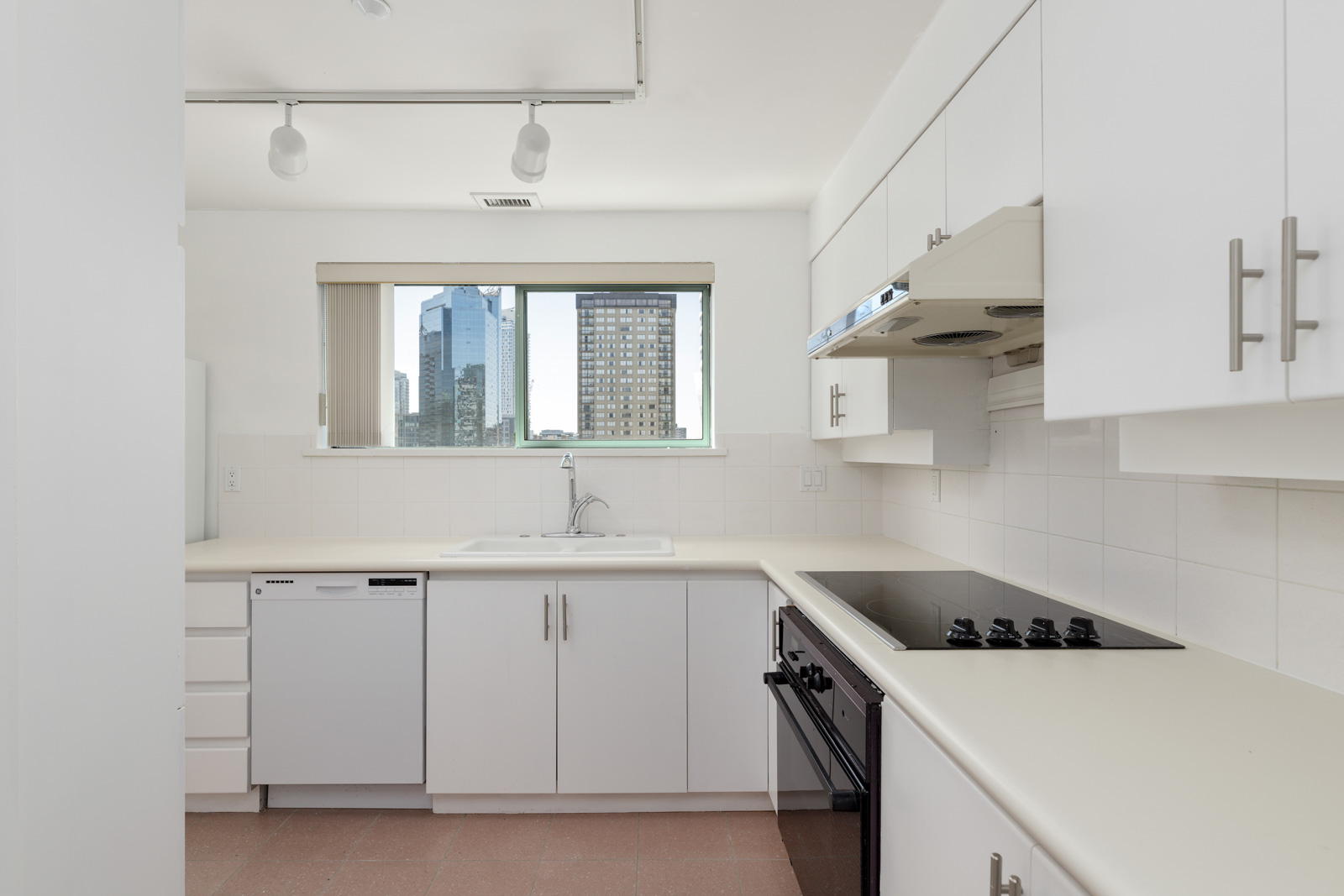 Modern kitchen with white cabinets, electric cooktop, built-in oven, dishwasher, and a large window with a cityscape view.