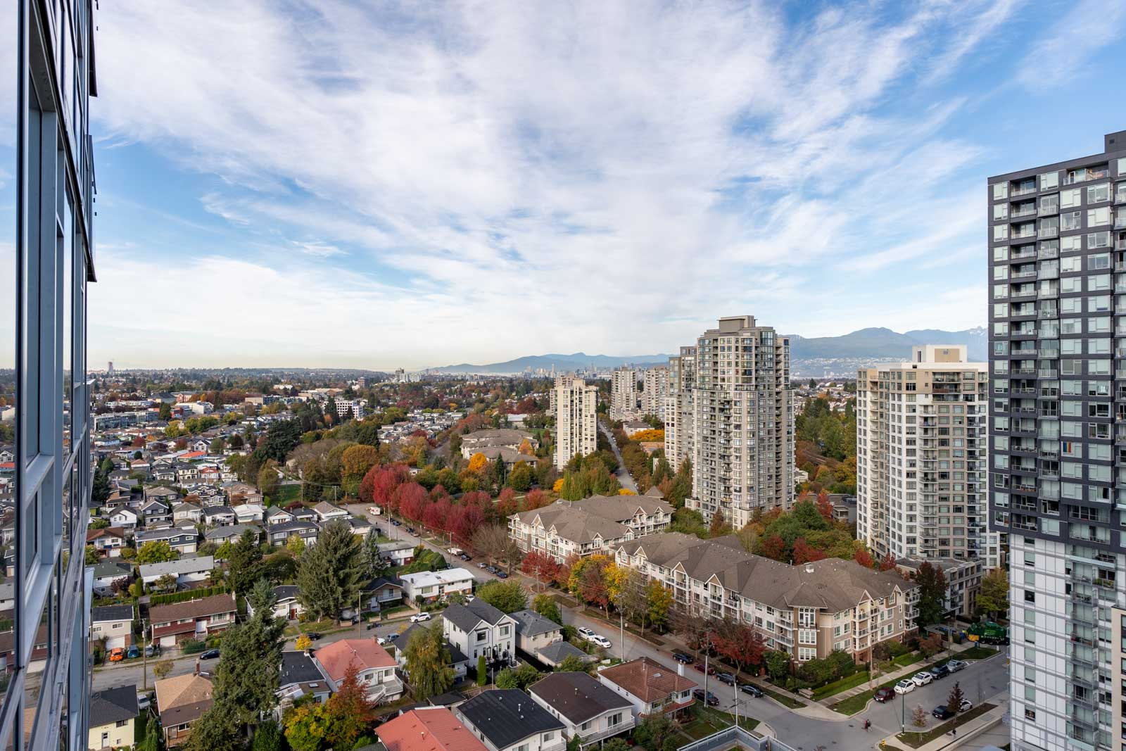 High-angle view of a cityscape with residential buildings, apartment towers, and trees in autumn colors under a partly cloudy sky.