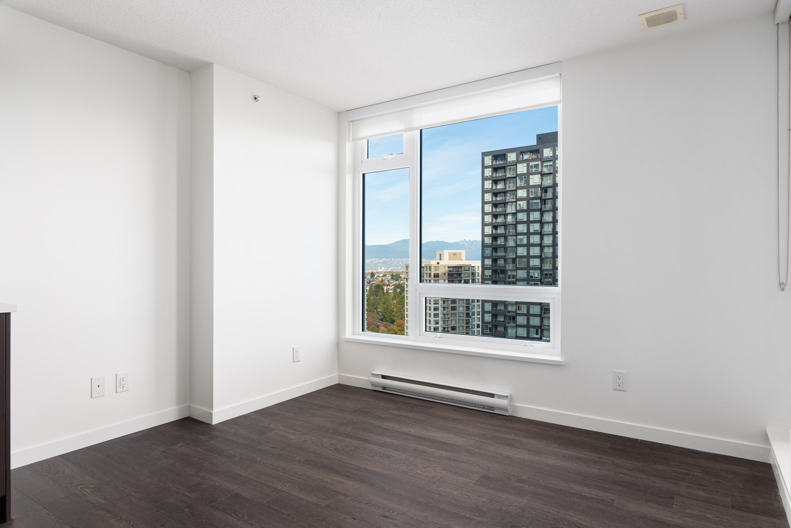 Unfurnished room with white walls, dark wood floor, large window with city view, and a baseboard heater under the window.