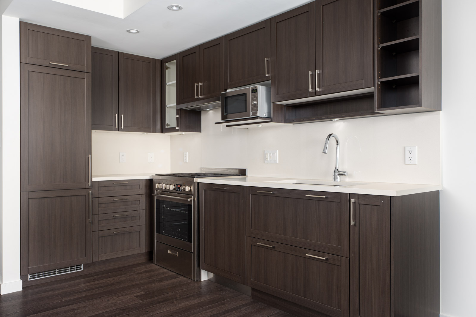 Modern kitchen with dark wood cabinets, built-in appliances, white countertops, and under-cabinet lighting.