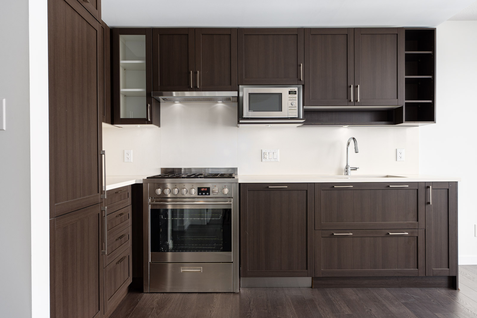 Modern kitchen with dark wood cabinets, stainless steel oven and microwave, white backsplash, and a sink with a sleek faucet.
