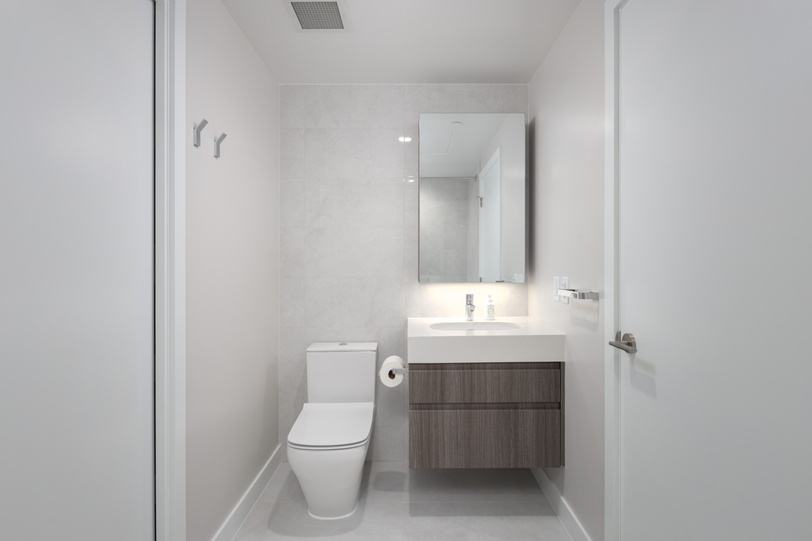 Modern bathroom with a wall-mounted sink vanity, a toilet, a large mirror, neutral walls, and minimal decor.