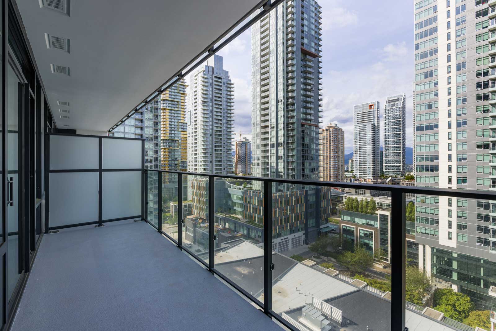 View from a high-rise balcony with glass railing, overlooking modern skyscrapers and urban buildings in a cityscape.