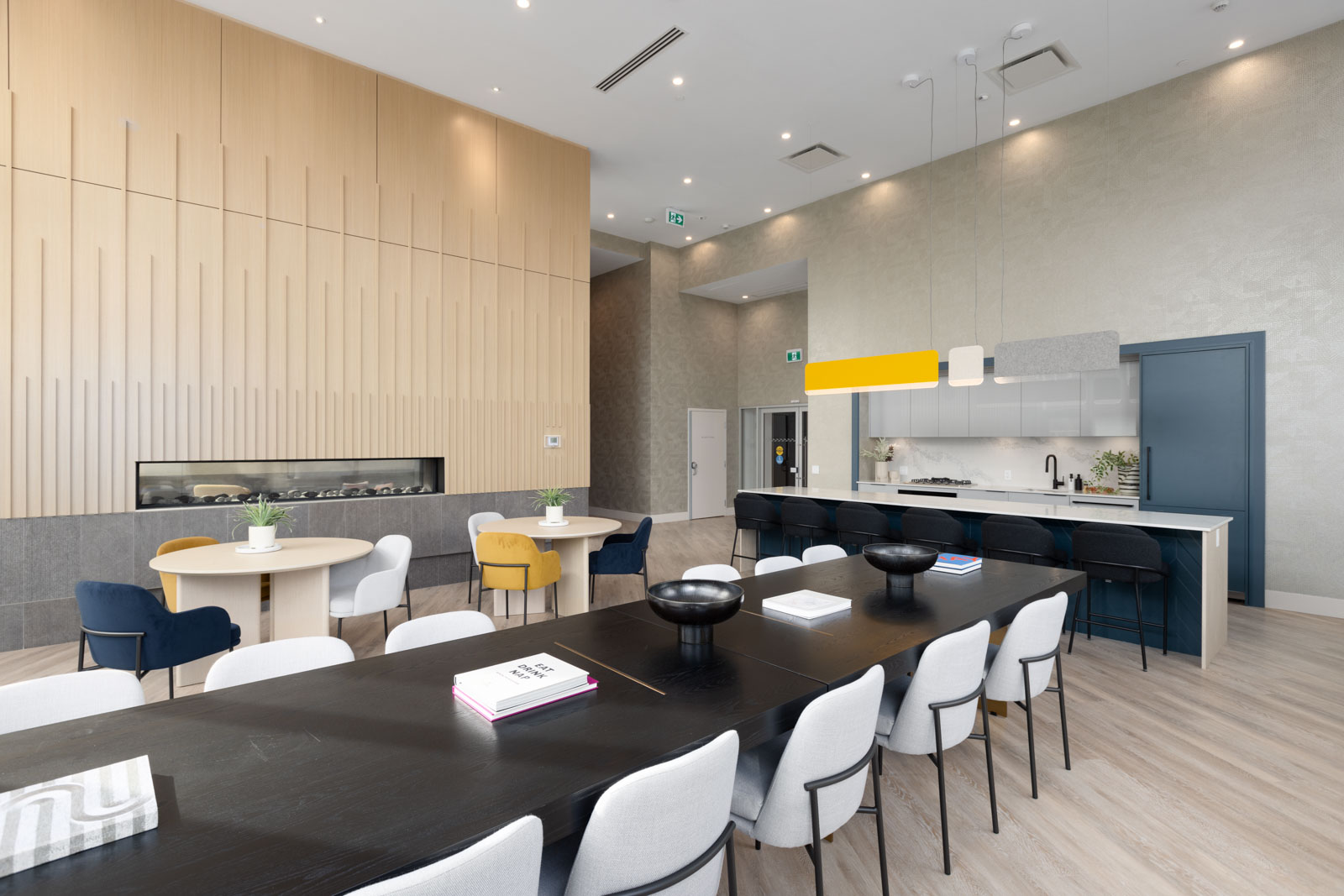 A modern, open-concept dining and kitchen area with light wood accents, black and white furniture, and a built-in fireplace along the wall.