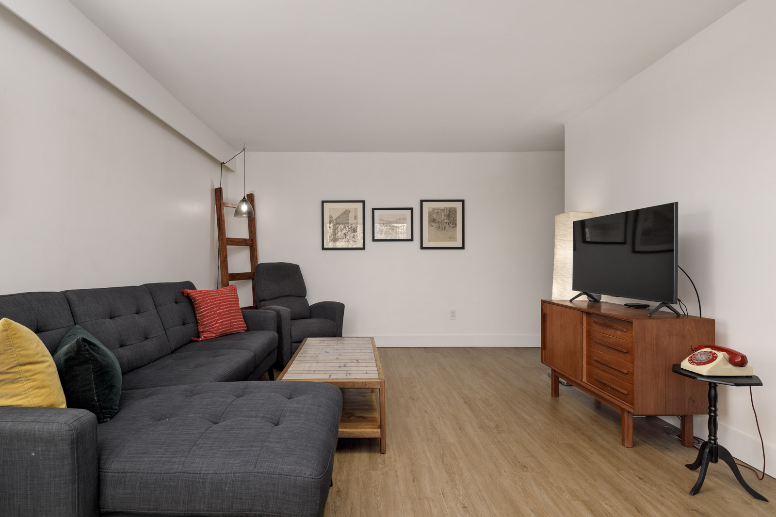 A modern living room with a gray sectional sofa, wooden coffee table, TV on a wooden console, and framed art on a white wall.