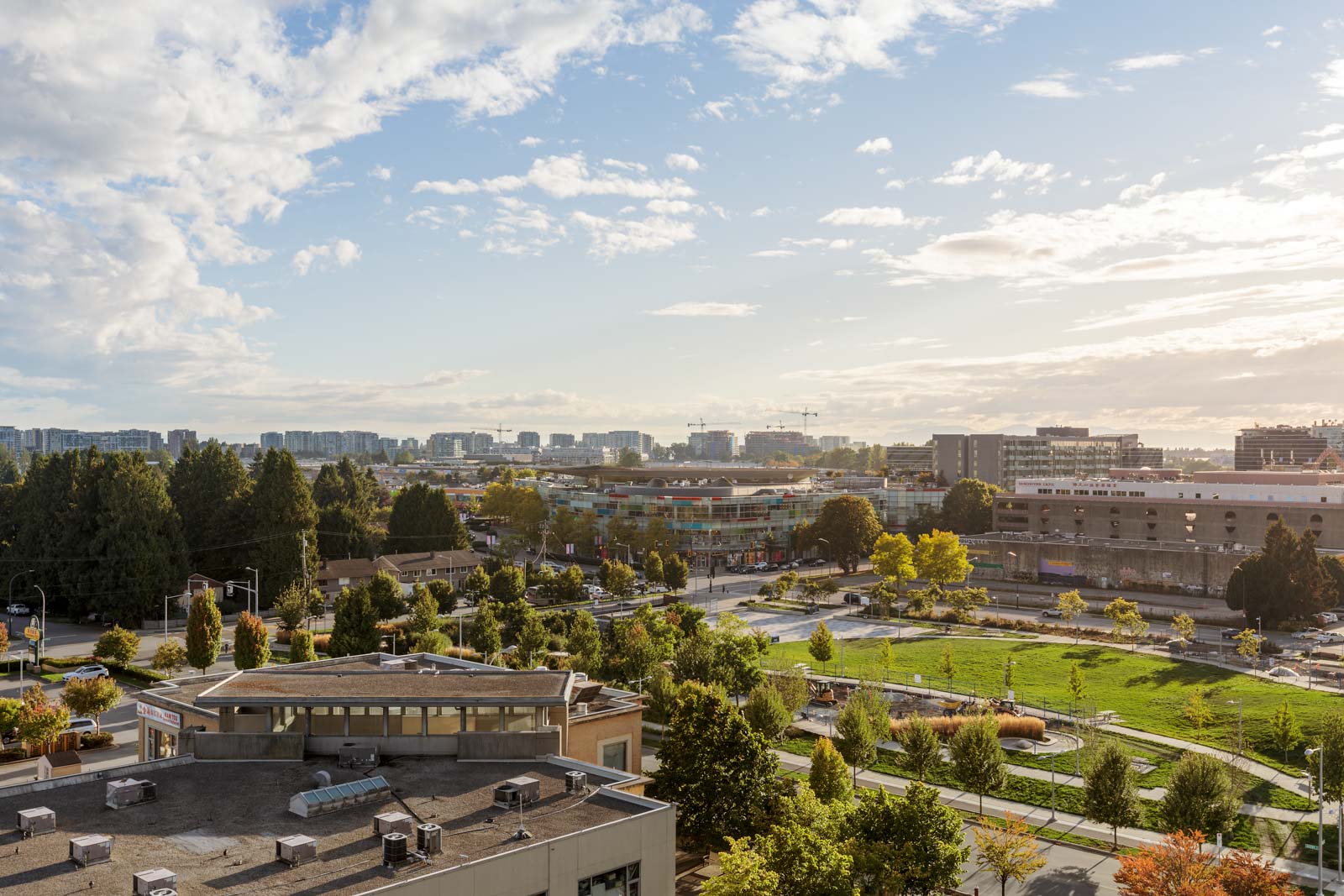 A cityscape view with green park space, buildings, and trees under a partly cloudy sky on a sunny day.