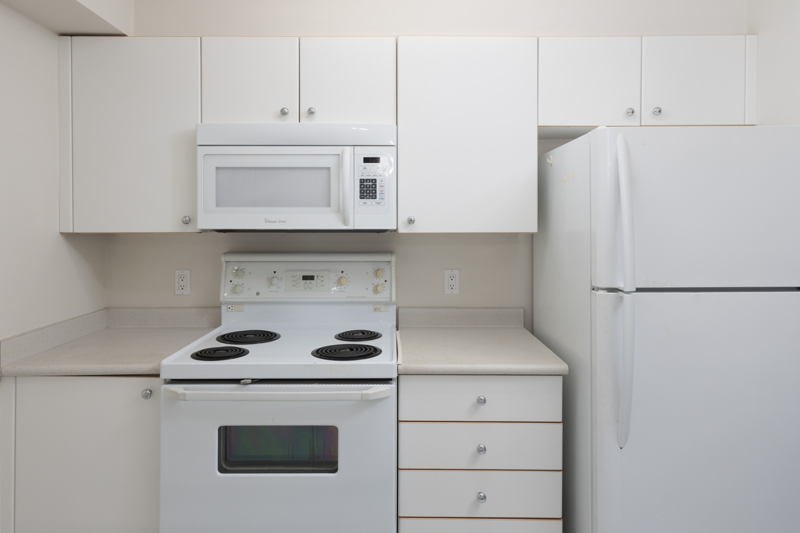 A small kitchen with white cabinets, an electric stove, a microwave above it, and a refrigerator on the right side.