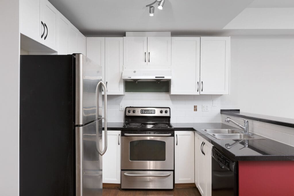 Modern kitchen with stainless steel appliances, white cabinets, black countertops, double sink, and electric stove under a white range hood.