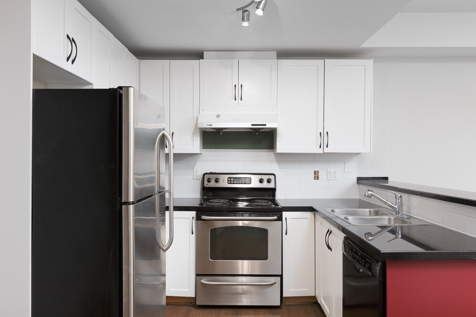 Modern kitchen with stainless steel appliances, white cabinets, black countertops, double sink, and electric stove under a white range hood.