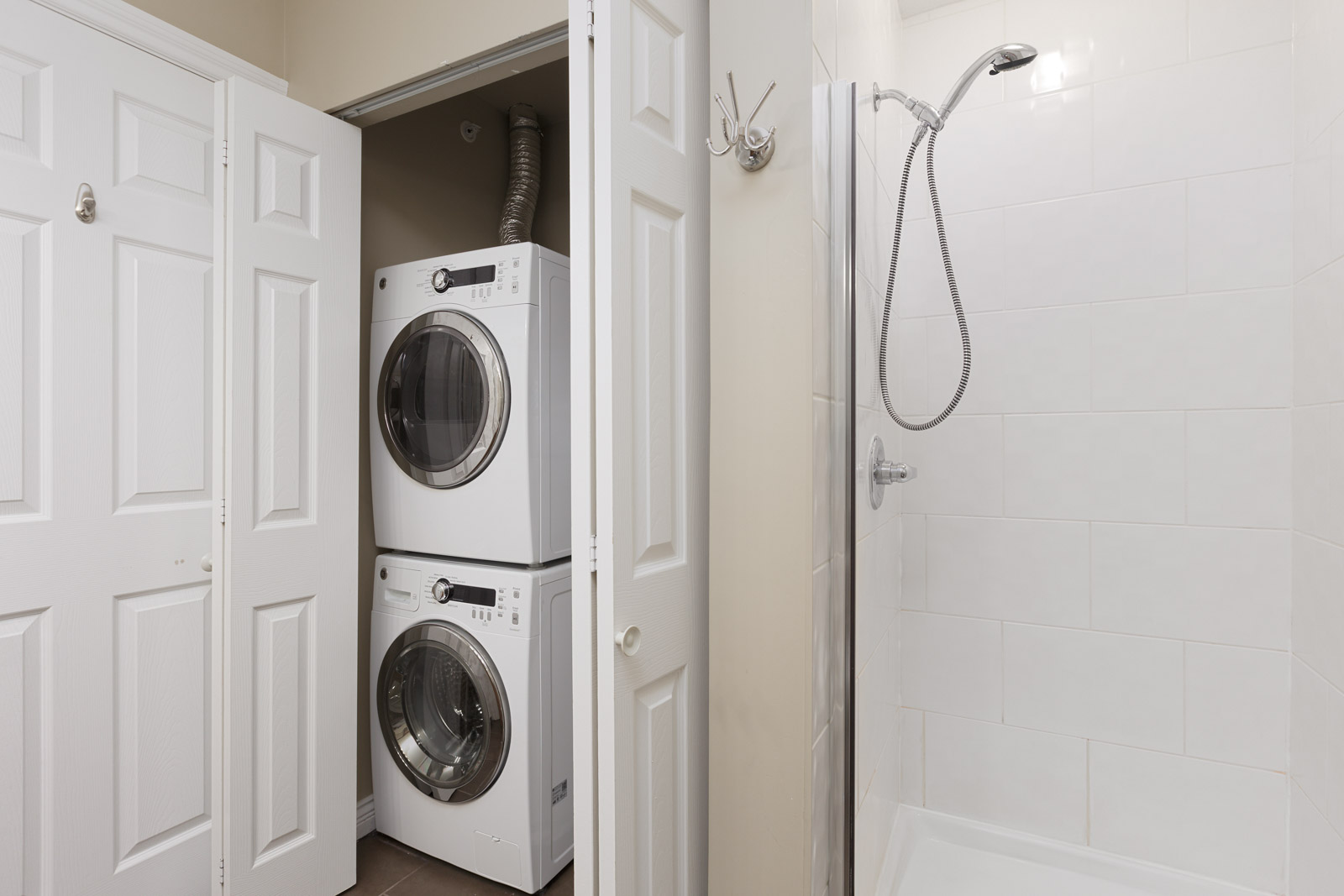 A bathroom with a white shower stall and a closet containing a stacked washer and dryer.