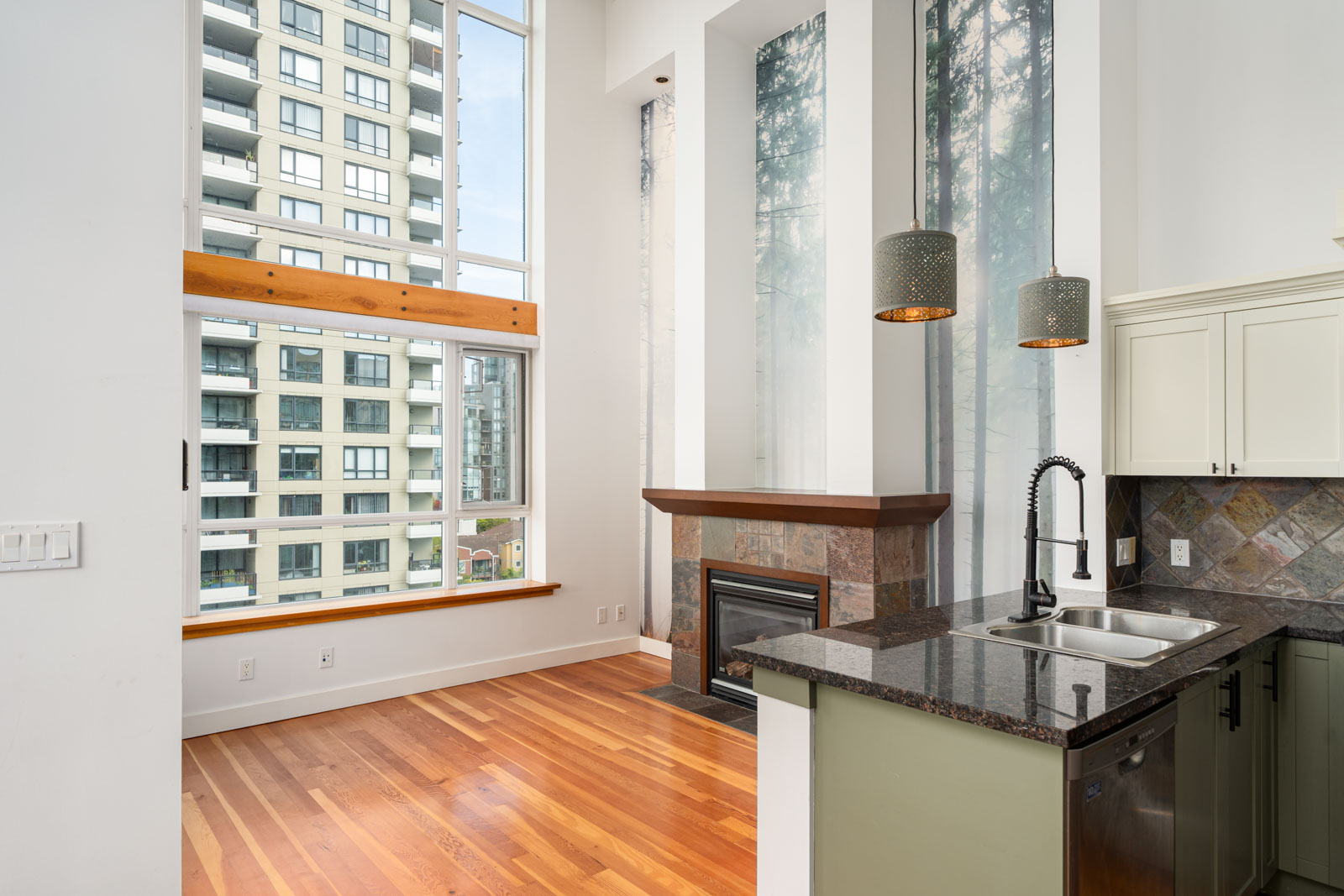 Modern apartment interior with large windows, hardwood floors, a kitchen island with sink, pendant lights, and a fireplace under high ceilings.